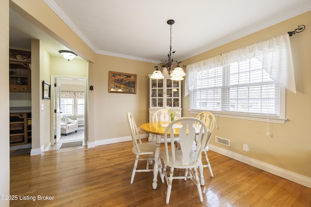 dining area featuring visible vents, a notable chandelier, ornamental molding, wood finished floors, and baseboards