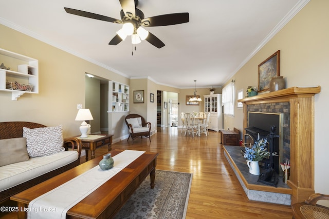 living room featuring ceiling fan with notable chandelier, light wood-type flooring, baseboards, and ornamental molding