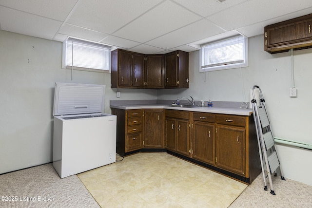 kitchen with light floors, a drop ceiling, a sink, light countertops, and dark brown cabinetry