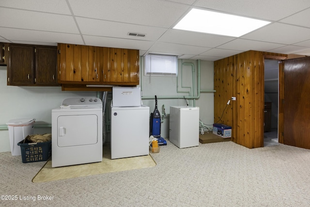 clothes washing area with visible vents, cabinet space, carpet, wooden walls, and washing machine and clothes dryer