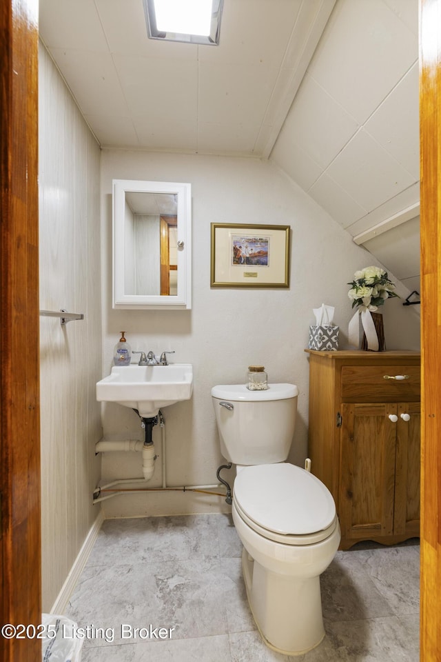 half bathroom with vaulted ceiling, toilet, and a sink