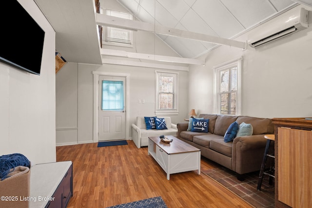 living area featuring lofted ceiling with beams, light wood-style flooring, and a wall unit AC