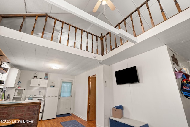 interior space featuring ceiling fan, light wood-style floors, and a towering ceiling