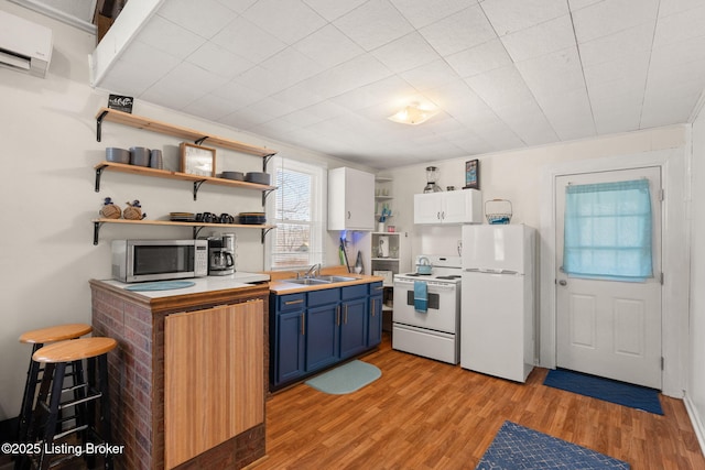 kitchen featuring blue cabinets, a wall mounted air conditioner, open shelves, a sink, and white appliances