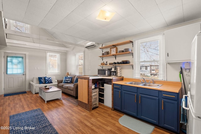 kitchen with an AC wall unit, blue cabinetry, stainless steel microwave, a sink, and light wood-style floors