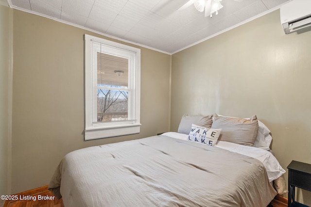 bedroom with crown molding, a wall mounted AC, baseboards, and wood finished floors