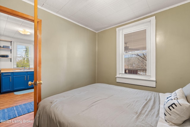 bedroom featuring crown molding, light wood-type flooring, and a sink