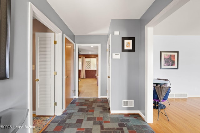 corridor featuring visible vents, baseboards, and dark wood-style flooring