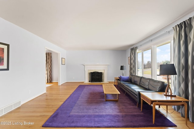 living room with a fireplace with flush hearth, baseboards, visible vents, and light wood finished floors