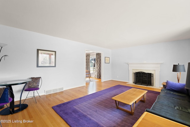 living area featuring visible vents, baseboards, a fireplace with flush hearth, and wood finished floors