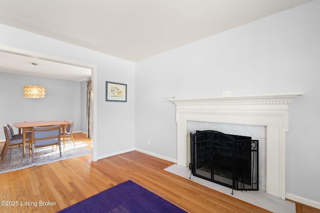 living area featuring a fireplace with flush hearth, baseboards, and wood finished floors