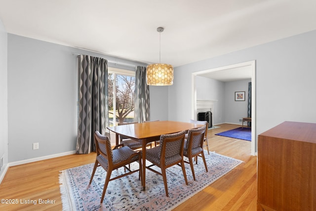 dining space featuring a fireplace with flush hearth, baseboards, and light wood-type flooring