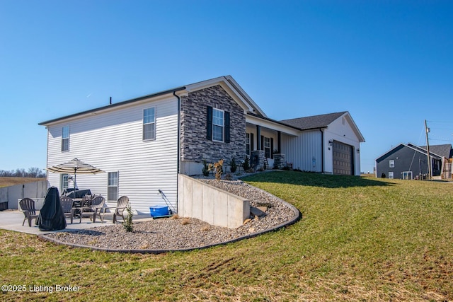 back of house with stone siding, an attached garage, a yard, and a patio