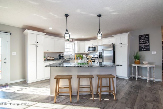 kitchen with a center island, dark stone counters, appliances with stainless steel finishes, white cabinets, and a sink