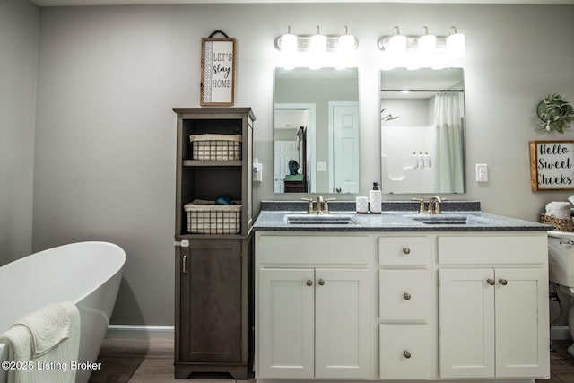 full bath with a sink, a freestanding tub, wood finished floors, and double vanity