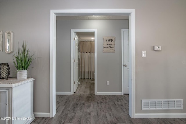 hall with wood finished floors, visible vents, and baseboards