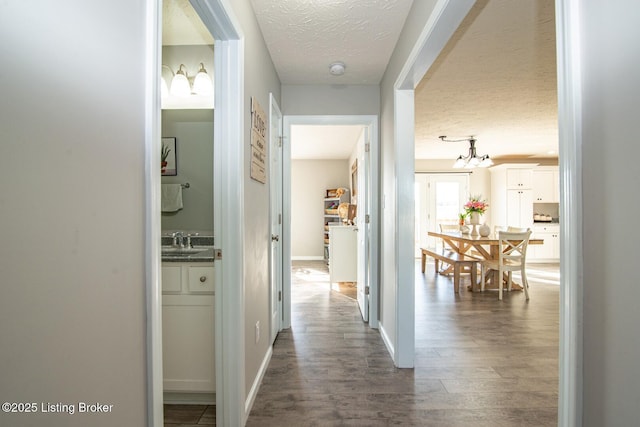 corridor featuring a sink, baseboards, a textured ceiling, and wood finished floors