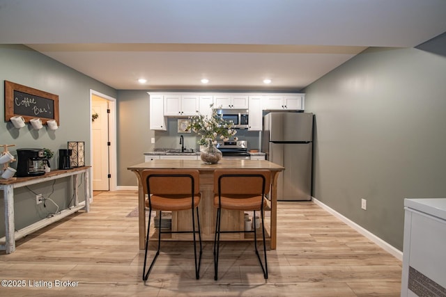 kitchen featuring light wood finished floors, a kitchen island, appliances with stainless steel finishes, white cabinetry, and a sink