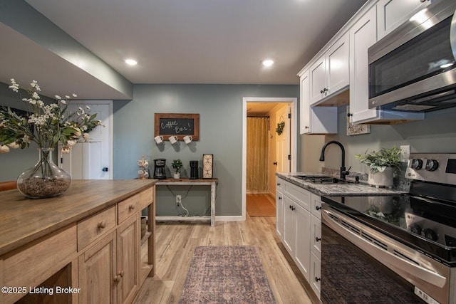 kitchen with a sink, stainless steel appliances, white cabinets, light wood-type flooring, and butcher block counters