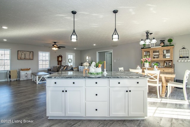 kitchen with decorative light fixtures, white cabinets, light stone countertops, and wood finished floors