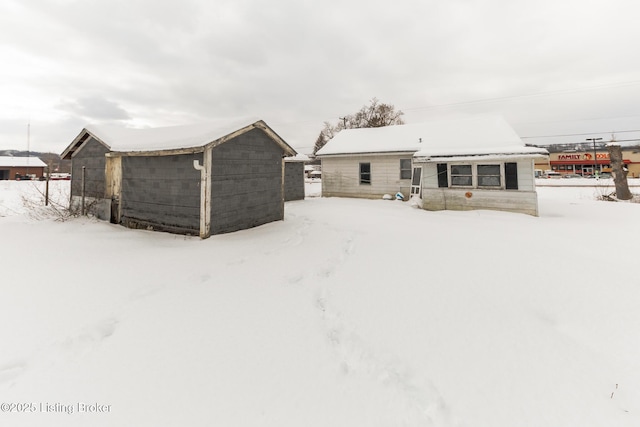 snow covered rear of property with a storage unit and an outdoor structure