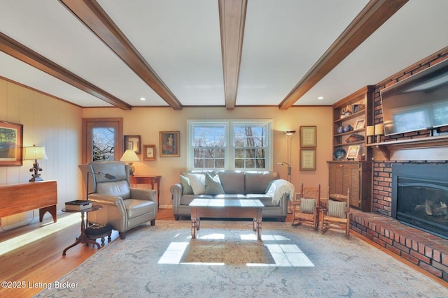 living area with beam ceiling, wood finished floors, a fireplace, and built in shelves