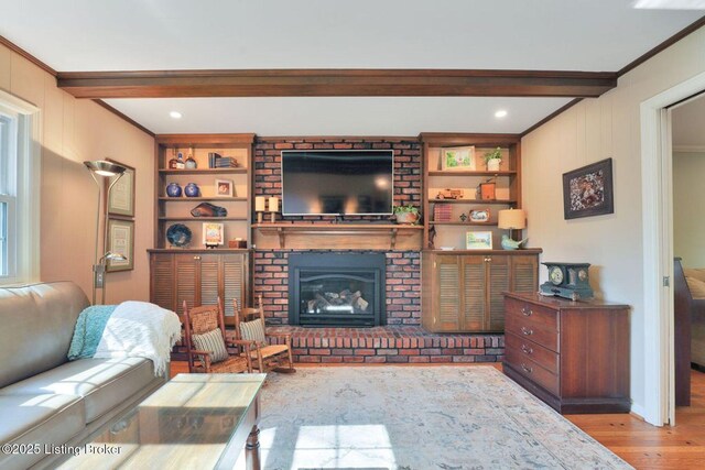 living area featuring built in features, wood finished floors, beam ceiling, ornamental molding, and a brick fireplace