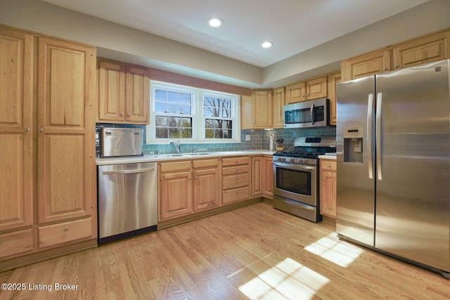 kitchen with light wood-style flooring, a sink, stainless steel appliances, light countertops, and decorative backsplash