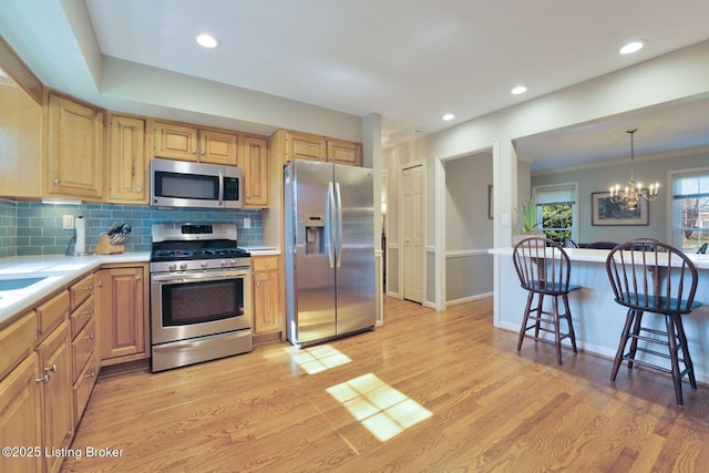 kitchen featuring an inviting chandelier, light wood-style flooring, light countertops, appliances with stainless steel finishes, and tasteful backsplash