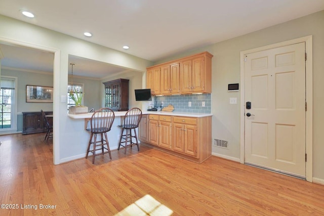 kitchen featuring baseboards, a breakfast bar, light wood-style flooring, light countertops, and backsplash