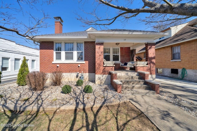 bungalow-style home featuring brick siding, a porch, a chimney, and roof with shingles