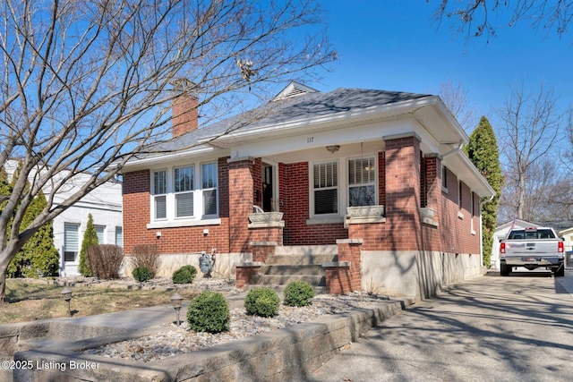 view of front of home with brick siding, driveway, and a chimney