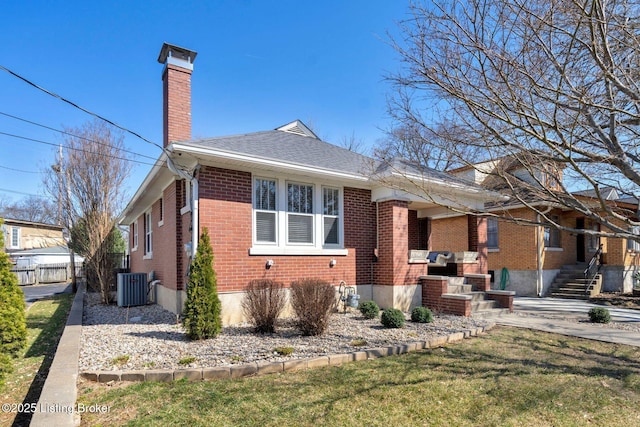 view of home's exterior featuring central air condition unit, a yard, roof with shingles, brick siding, and a chimney