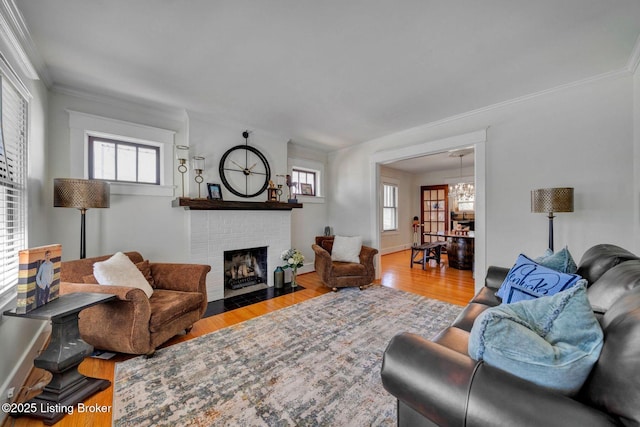 living room with wood finished floors, baseboards, a fireplace, ornamental molding, and a notable chandelier