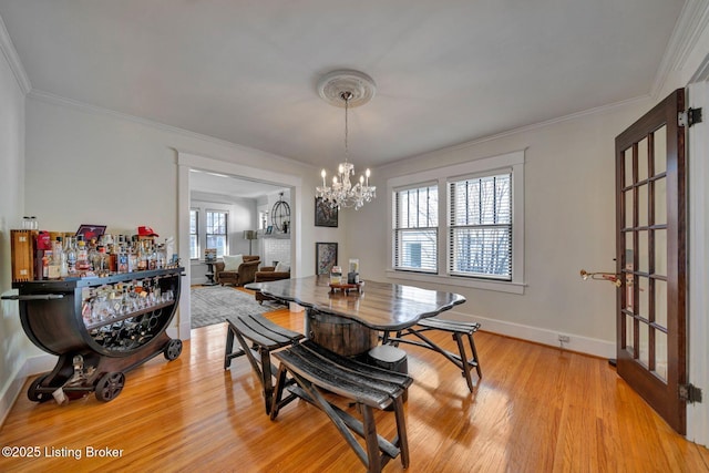 dining space featuring light wood-style floors, baseboards, a notable chandelier, and ornamental molding