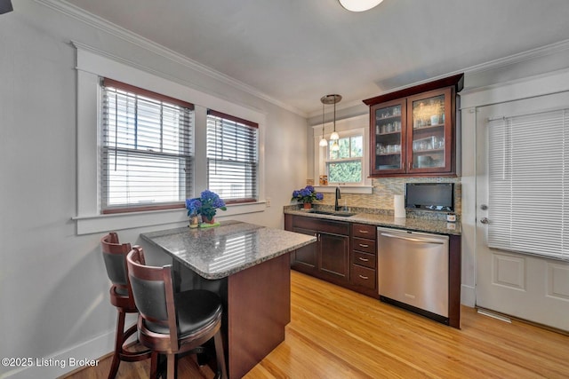 kitchen featuring light wood finished floors, glass insert cabinets, ornamental molding, stainless steel dishwasher, and a sink