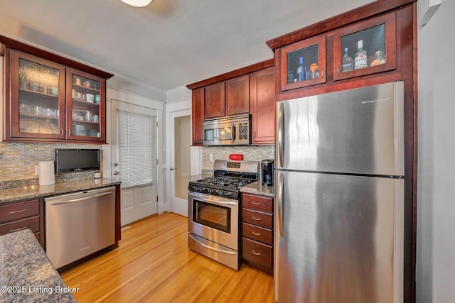 kitchen featuring glass insert cabinets, light wood-type flooring, ornamental molding, decorative backsplash, and stainless steel appliances