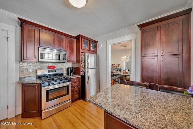 kitchen with backsplash, crown molding, light wood-style flooring, an inviting chandelier, and stainless steel appliances