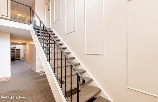 stairway featuring baseboards, a high ceiling, and carpet