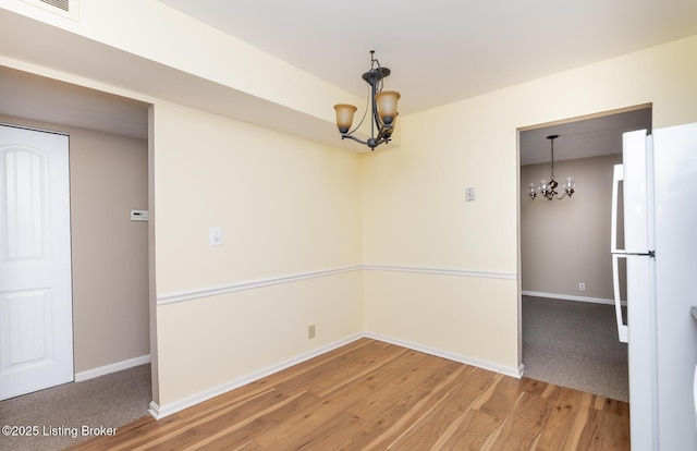 unfurnished dining area featuring a notable chandelier, baseboards, and wood finished floors