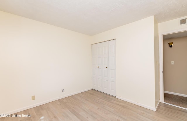 unfurnished bedroom with a closet, a textured ceiling, light wood-type flooring, and baseboards