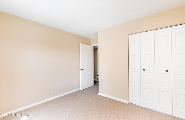 unfurnished bedroom featuring light colored carpet, baseboards, a closet, and a textured ceiling