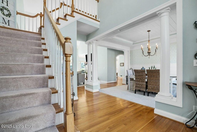 stairway with decorative columns, wood finished floors, and a chandelier