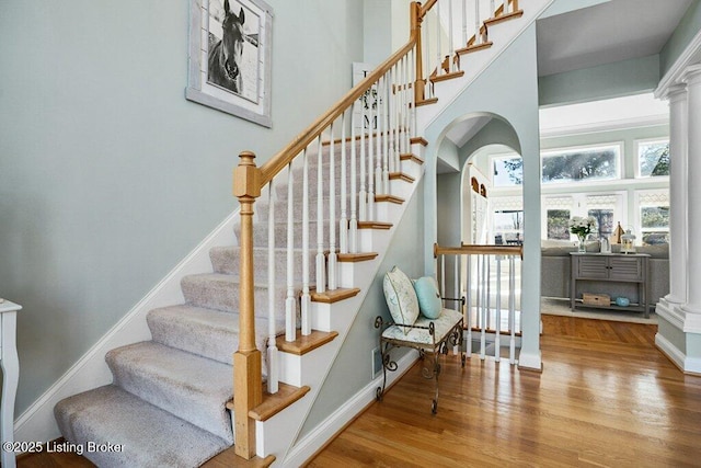 stairs featuring wood finished floors, baseboards, ornate columns, and arched walkways