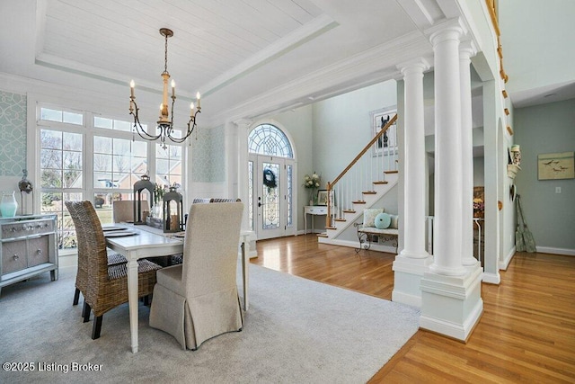 dining space with a raised ceiling, decorative columns, wood finished floors, and a chandelier