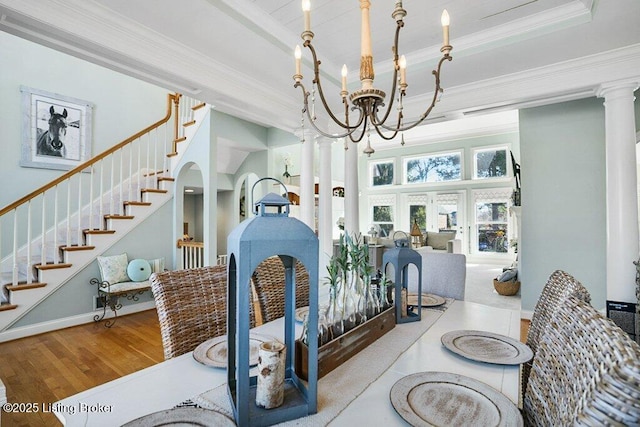 dining area featuring wood finished floors, an inviting chandelier, a tray ceiling, ornamental molding, and stairs