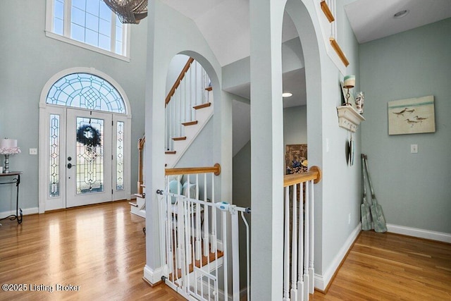 foyer featuring stairway, wood finished floors, baseboards, arched walkways, and a towering ceiling