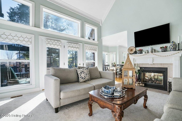 carpeted living area featuring high vaulted ceiling, a fireplace, visible vents, and ornamental molding