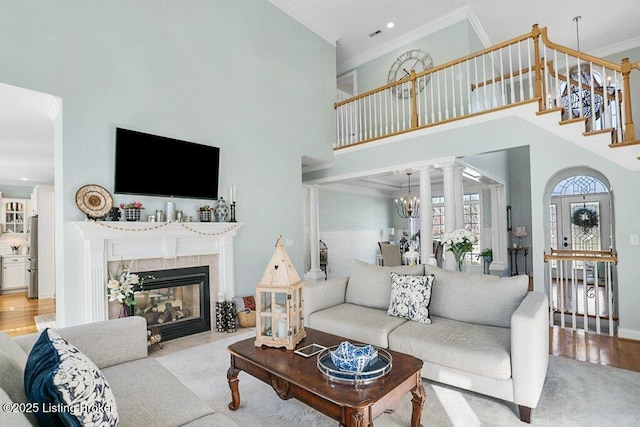 living area featuring stairway, wood finished floors, a high ceiling, a tile fireplace, and ornamental molding