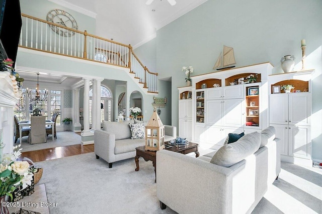 living area with light wood-style flooring, crown molding, an inviting chandelier, and decorative columns